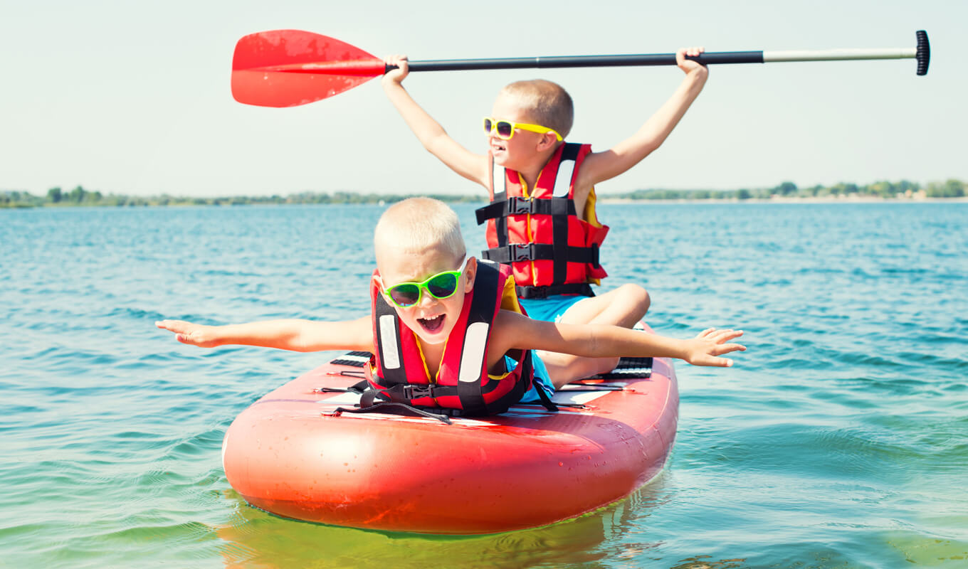 Two kids on a life jacket riding a paddle board
