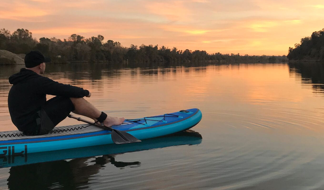 Man on an SUP wearing SUP ankle leash while watching sunset