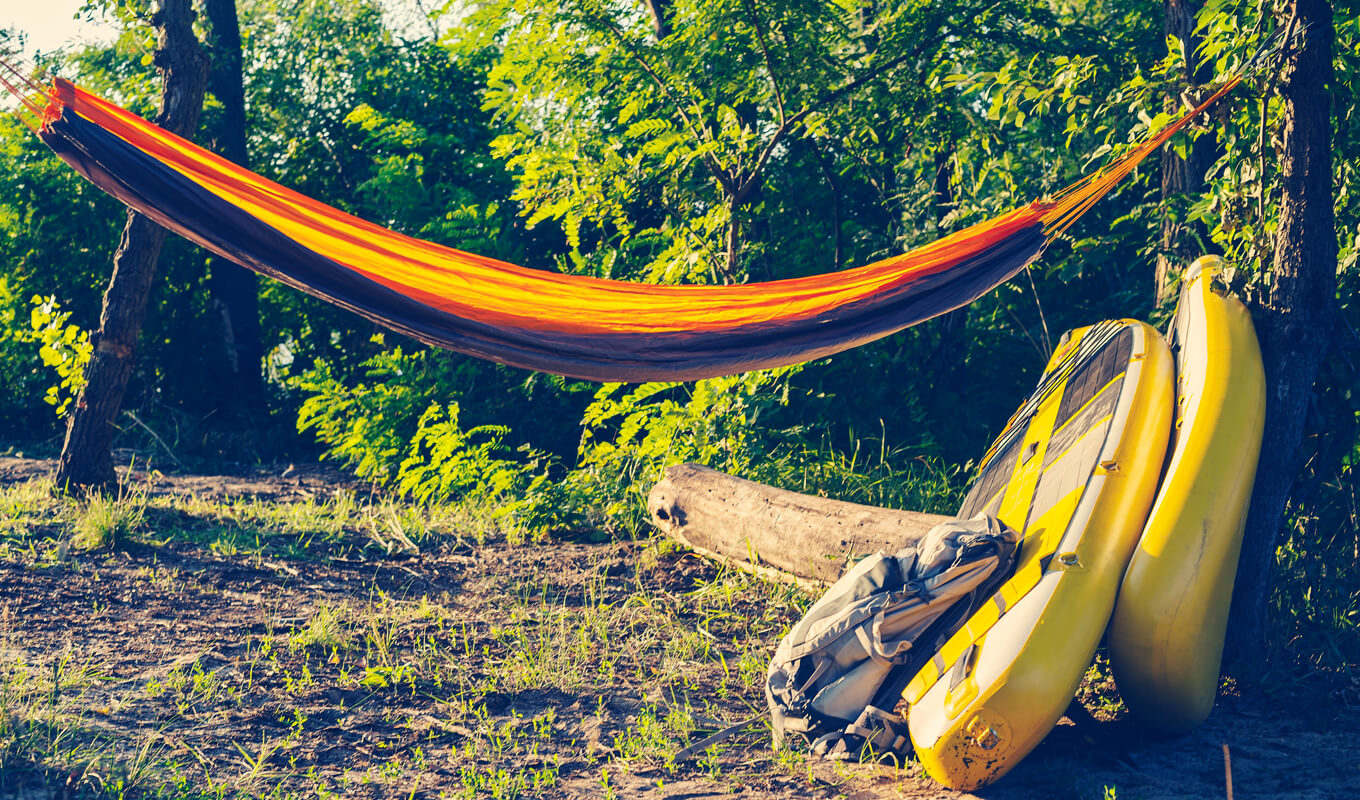 Aufblasbares Paddelbrett in der Nähe einer Hängematte auf einem SUP-Camping