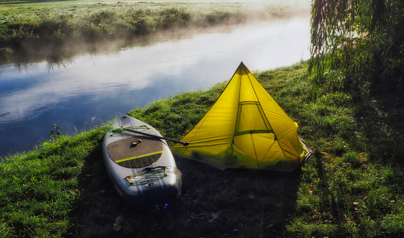 Inflatable paddle board near a camping tent