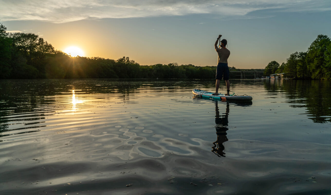 Man paddle boarding on a river at nightfall