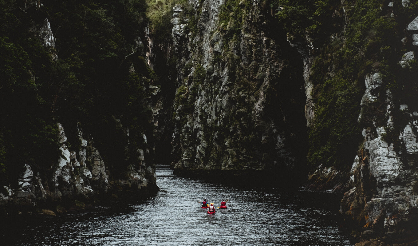 People kayaking in river between mountains