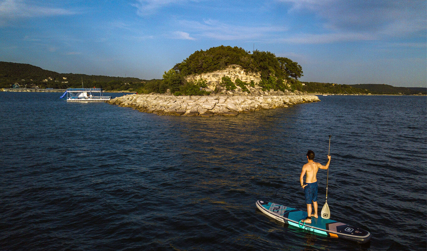 Man paddle boarding near an island with a boat dock