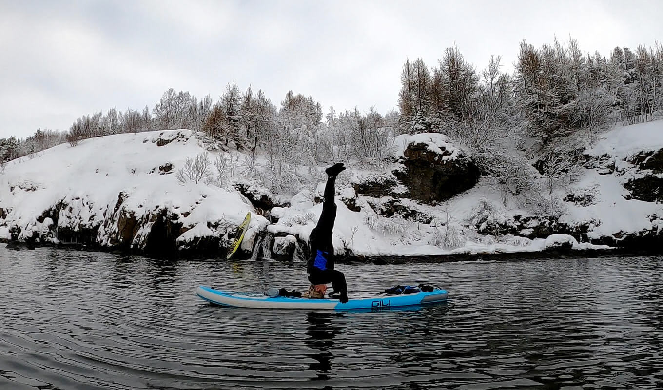 Woman wearing winter clothes performing Yoga on her inflatable paddle board