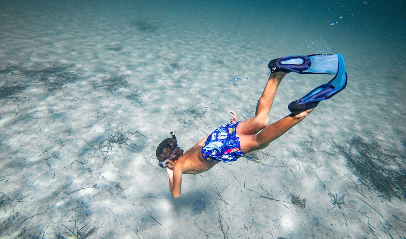 Kid on a blue short snorkeling