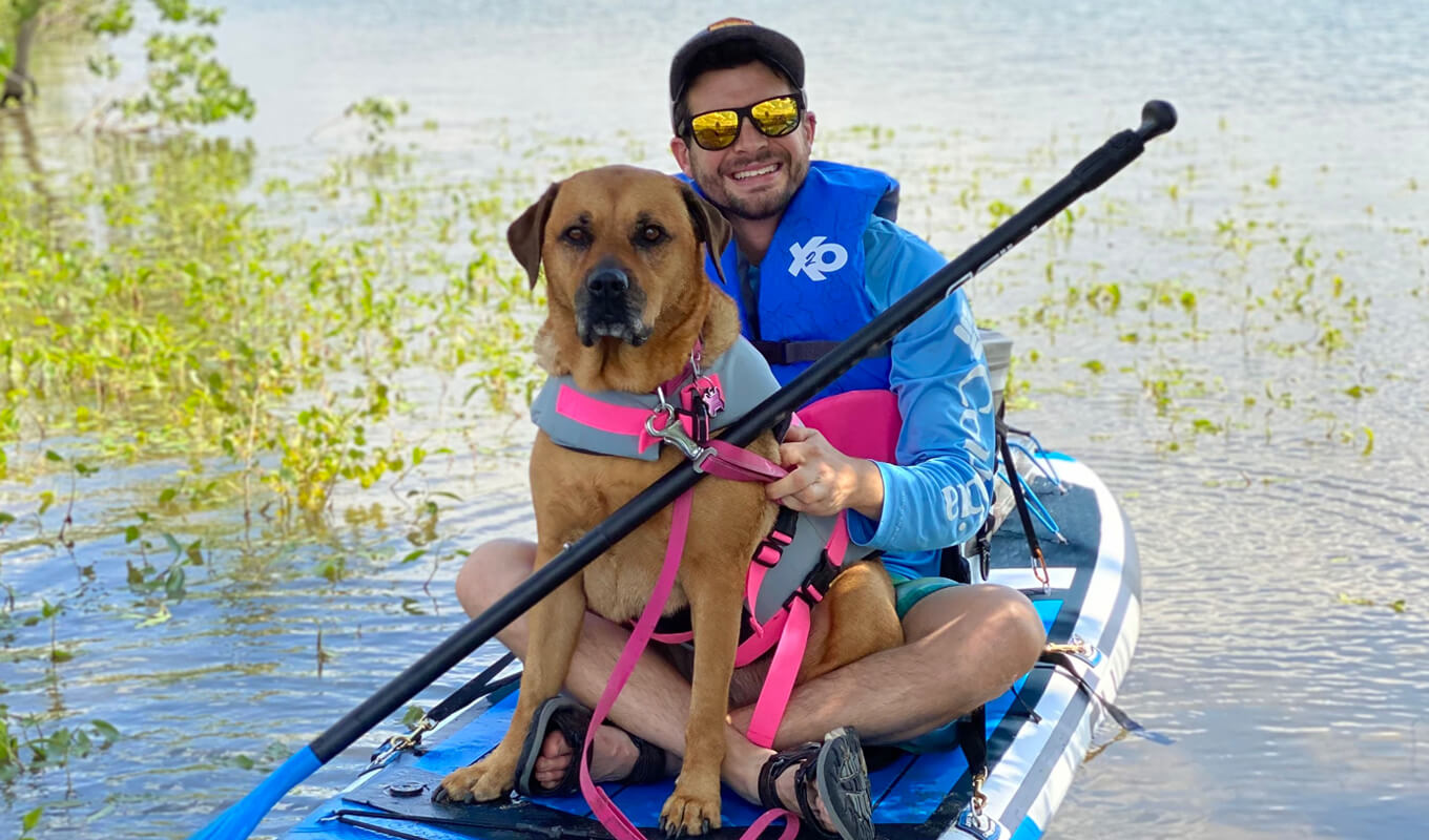 Mann und sein Hund tragen Schwimmwesten auf einem Paddelbrett