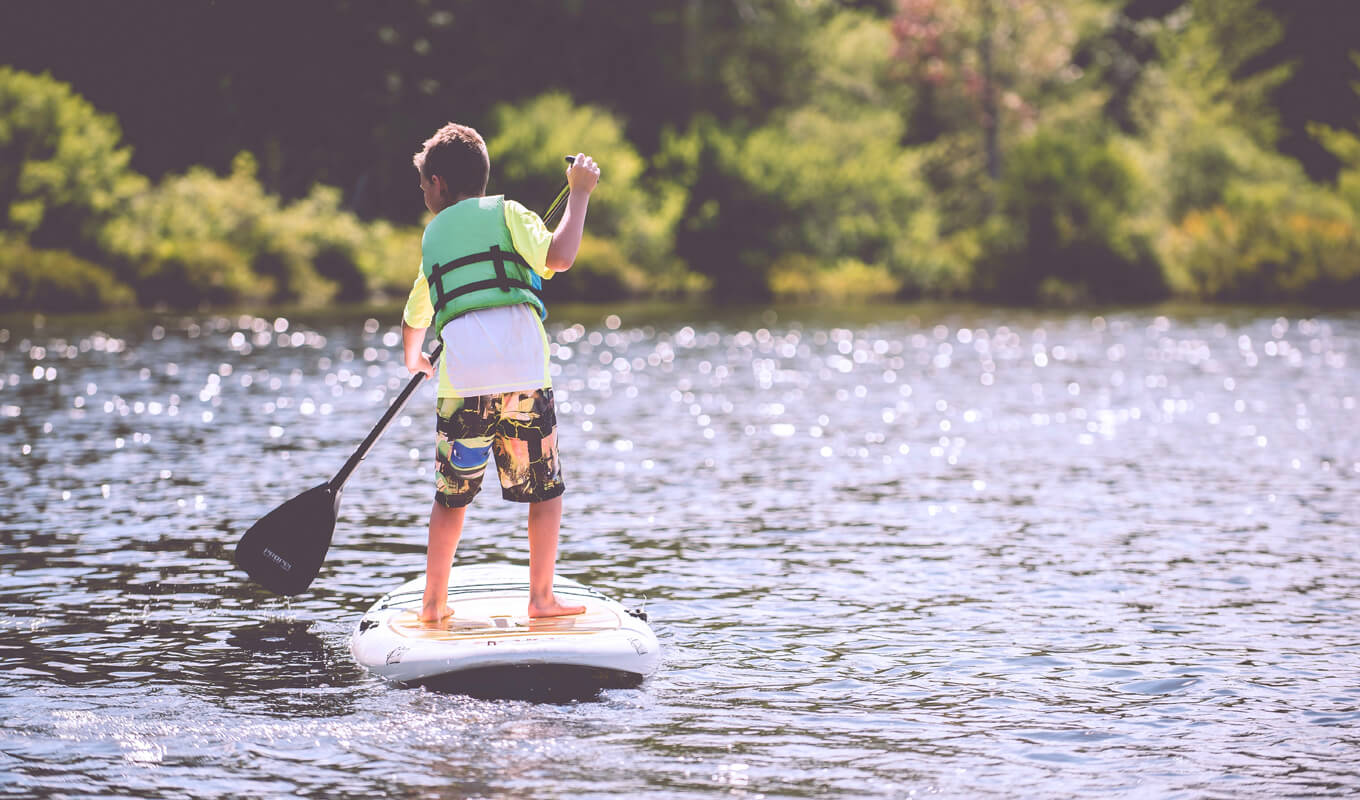 Kind mit Schwimmweste beim Paddle-Boarding