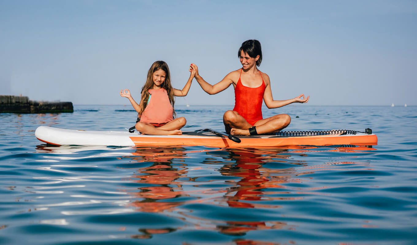 Mutter und Tochter machen Yoga auf einem Paddelbrett