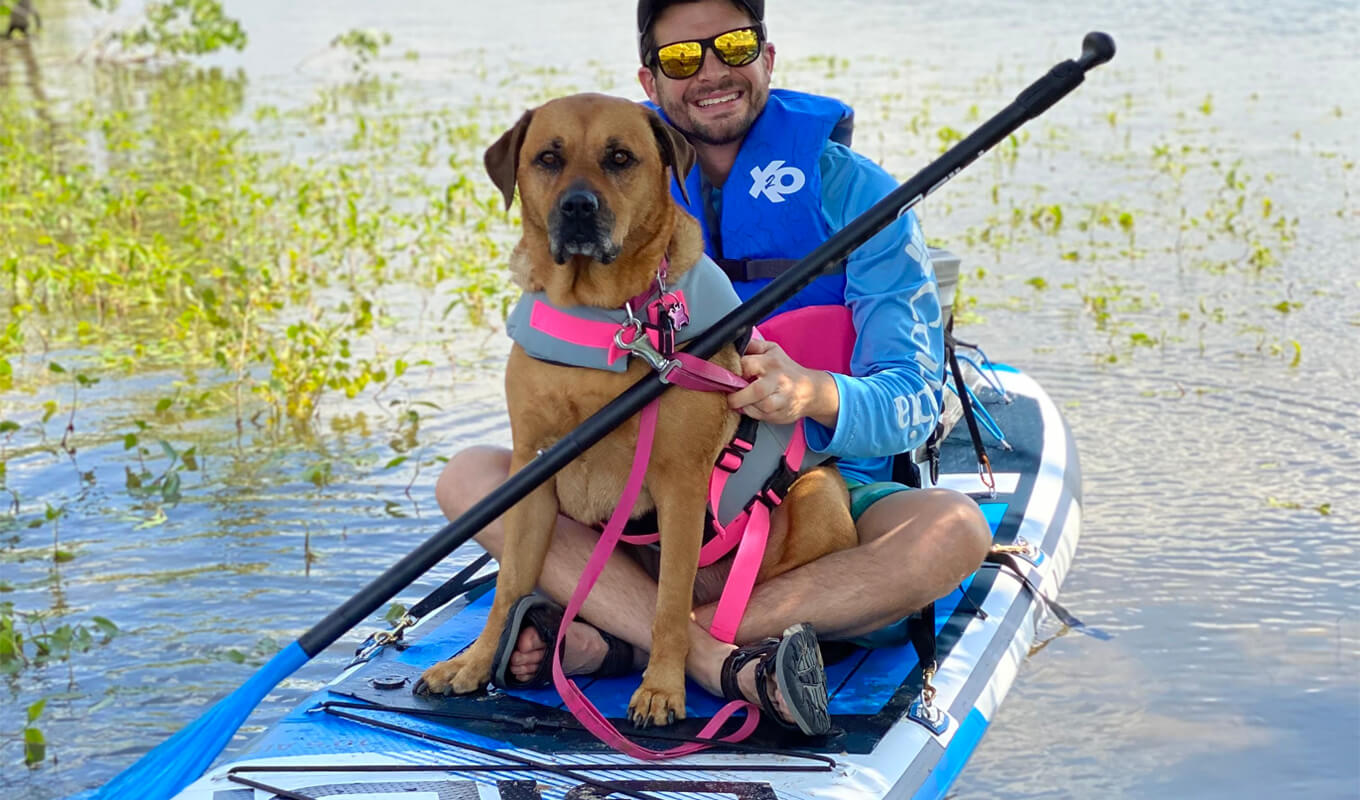 Man wearing a rashguard while paddle boarding with his dog