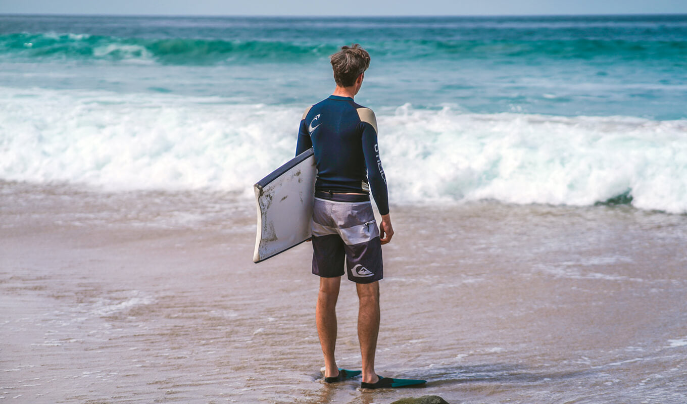 Man wearing a rashguard on beach while holding a boogie board
