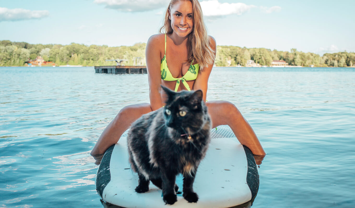 Woman on a green bikini with a cat on a stand up paddle board