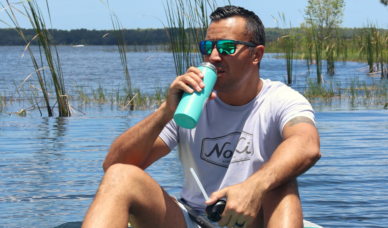 Vater trägt eine Sonnenbrille Trinkwasser beim Paddle-Boarding