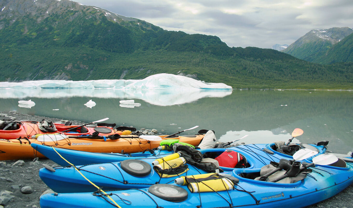 sit in kayaks on a lake near an ice berg