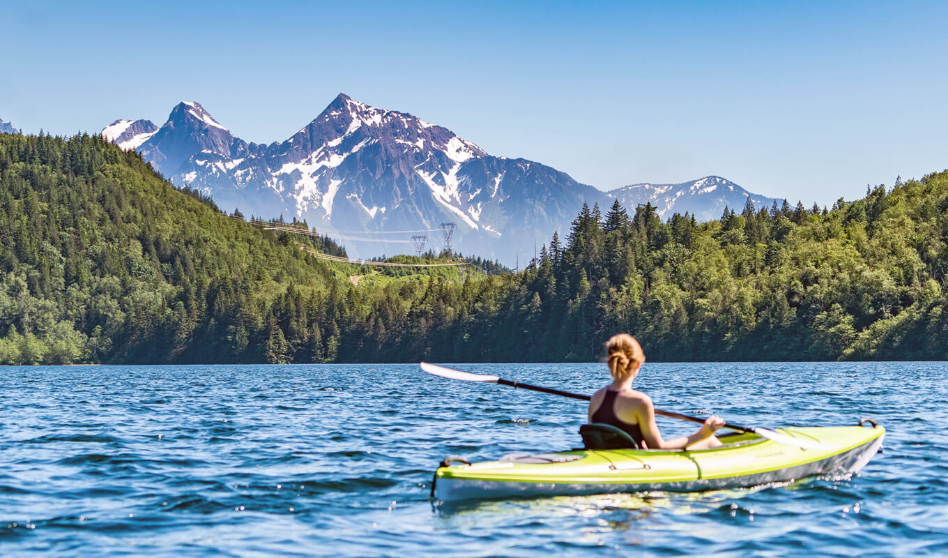 Woman kayaking on a lake with a view of snow capped mountain