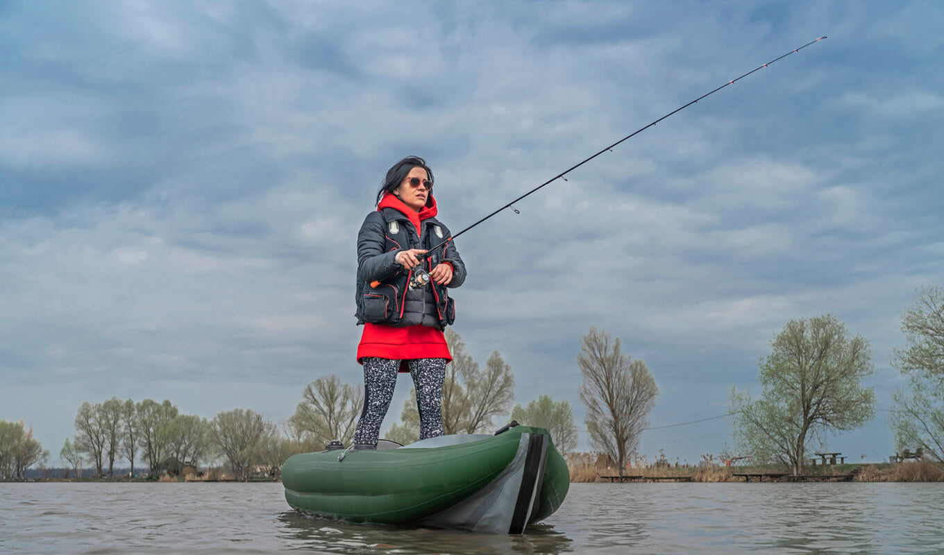 Woman on a green jacket standing while fishing on an inflatable kayak