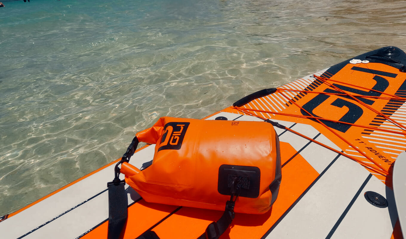 Orange waterproof roll top dry bag on a paddle board