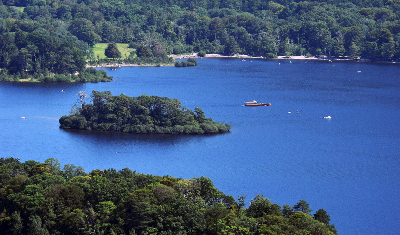 Rotes Boot in der Nähe einer Insel mit grünen Bäumen, umgeben von Derwentwater, Lake District