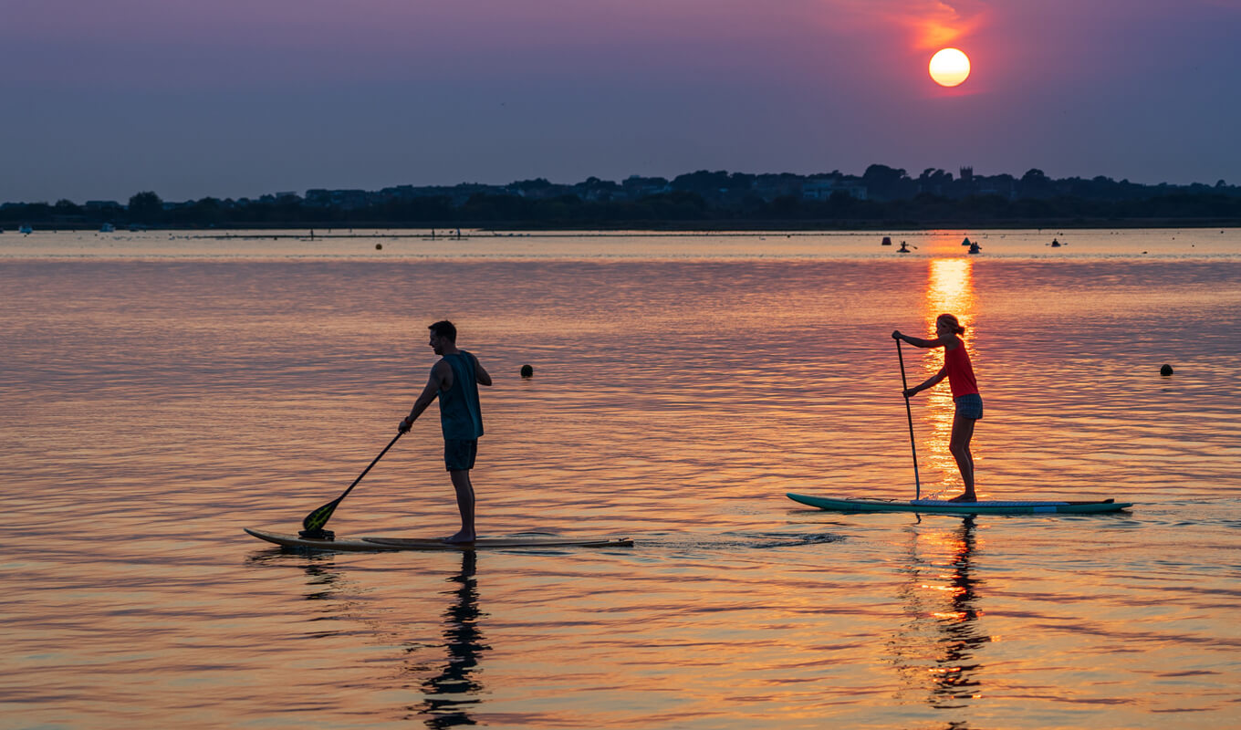 Man and a woman paddle boarding while sunset