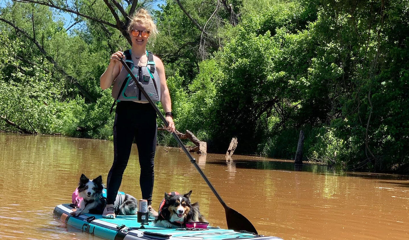 Woman wearing a Onyx MoveVent paddle boarding with her dogs