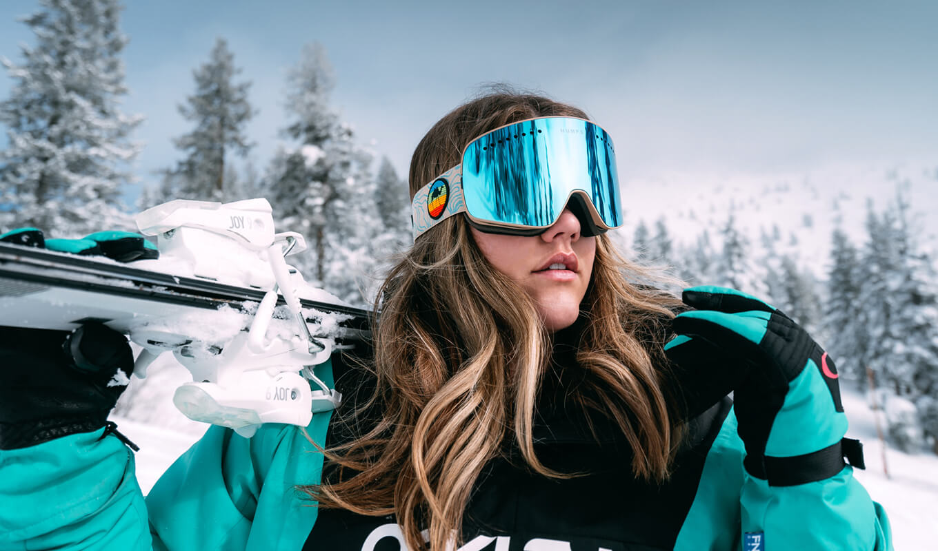 Woman wearing a black and teal jacket and snow boarding goggles