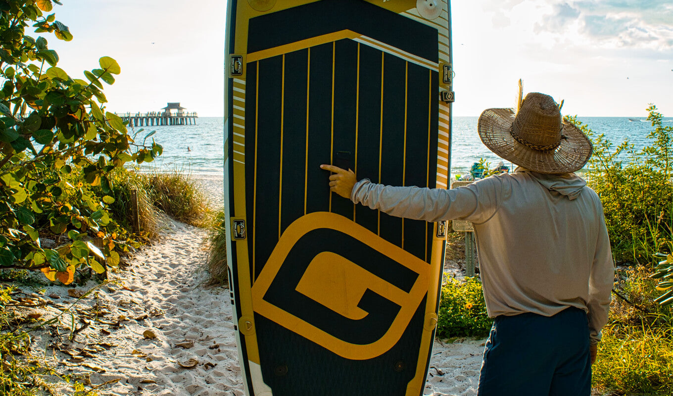 Man wearing a long sleeves and a hat while holding his GILI inflatable paddle board on the beach