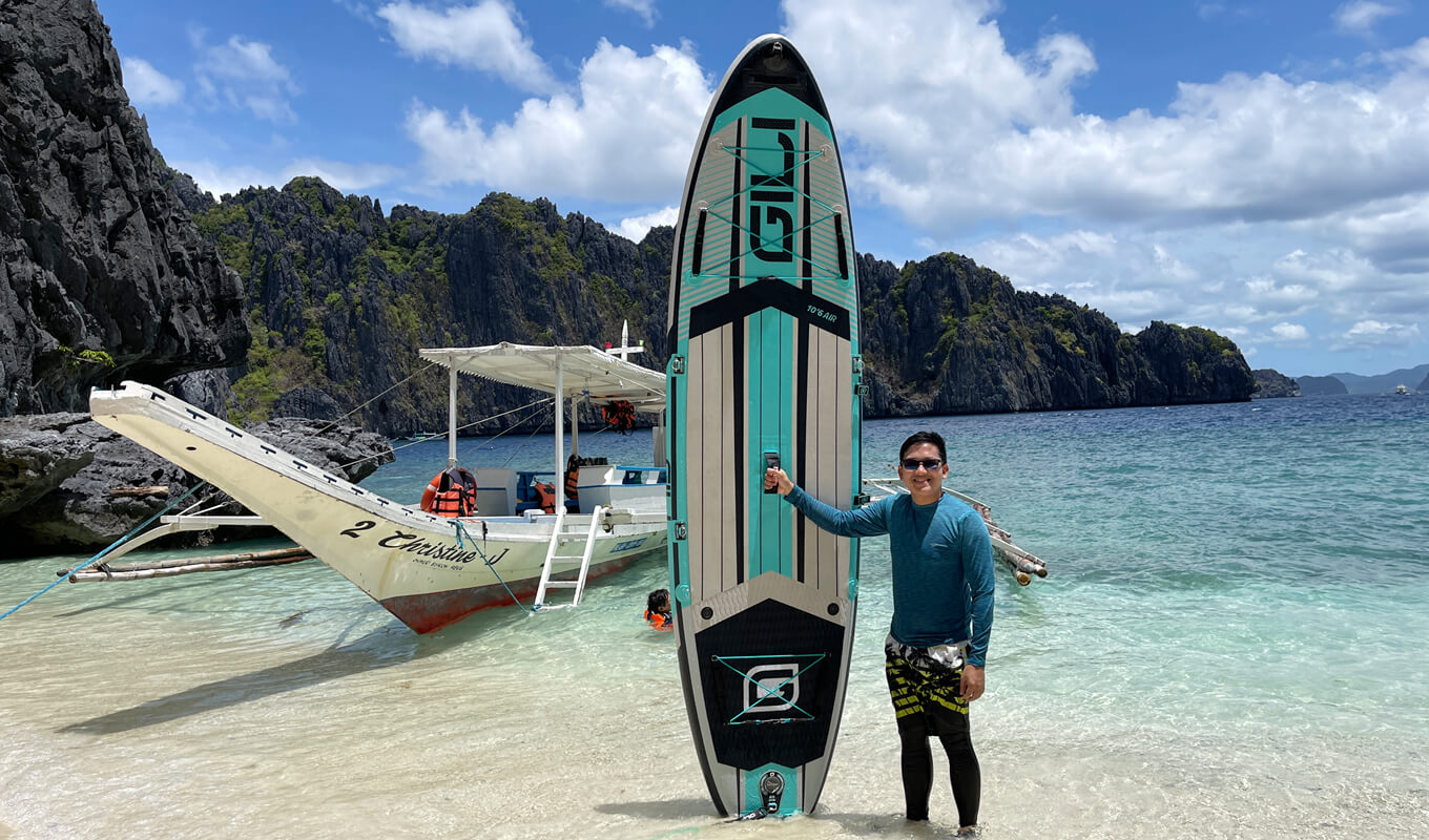 Man holding a paddle board on the sea with a boat as a background