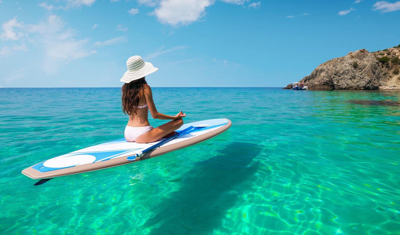 Woman meditating on a soft top paddle board