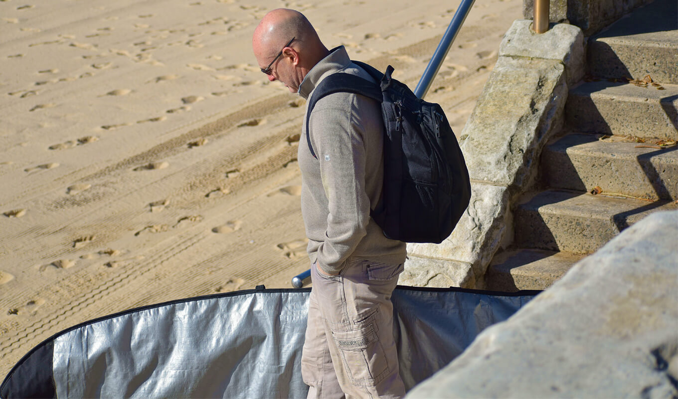 Man walking while holding a surfboard in a travel bag