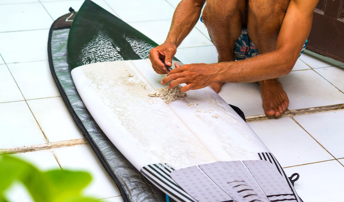 Man unwaxing a surfboard before putting on a surfboard bag
