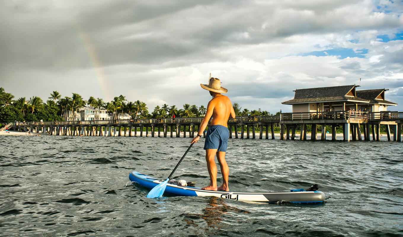 Mann auf einem blauen kurzen Paddle-Boarding im Ozean