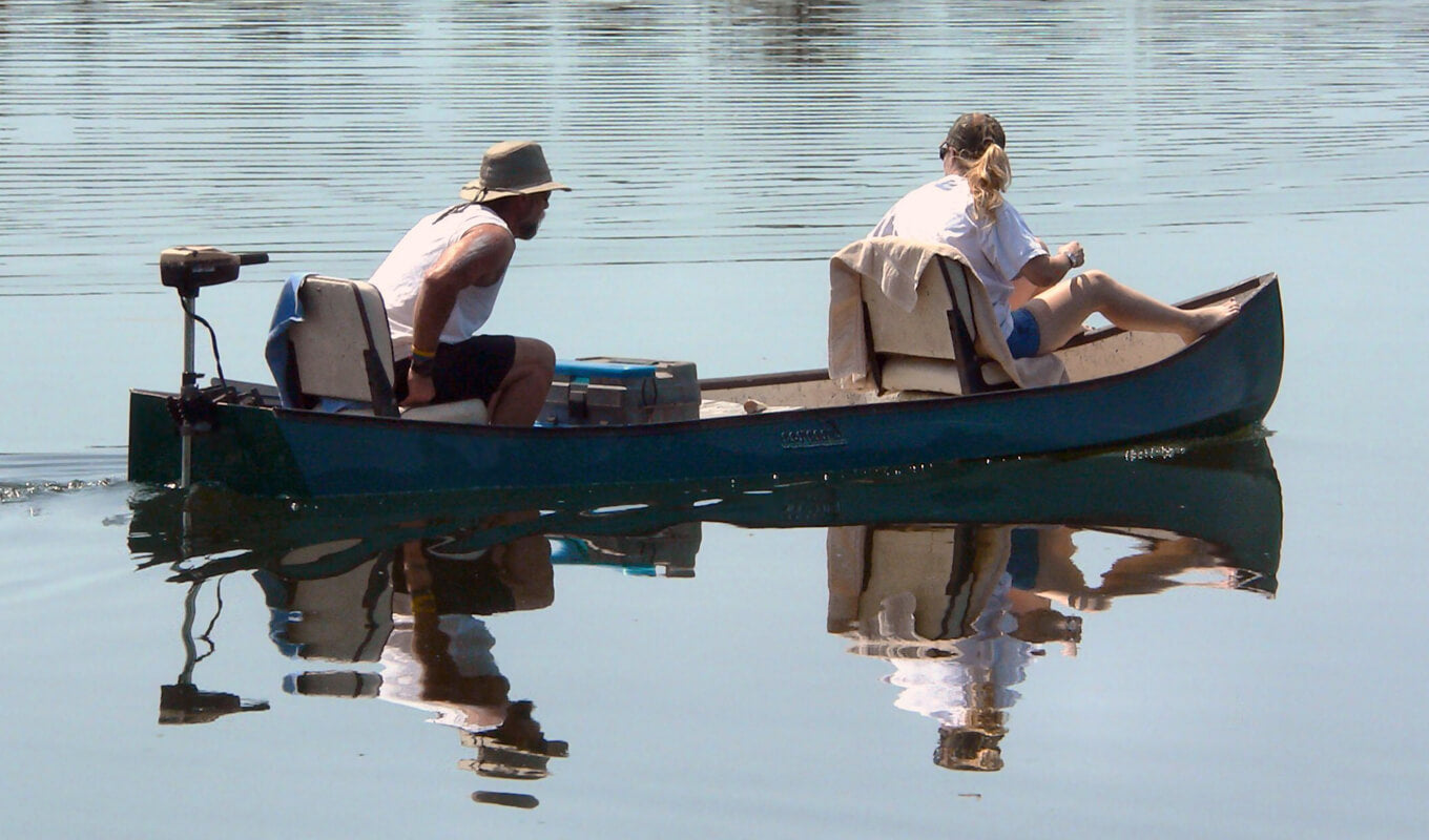 Man and a woman riding a boat with a trolling motor