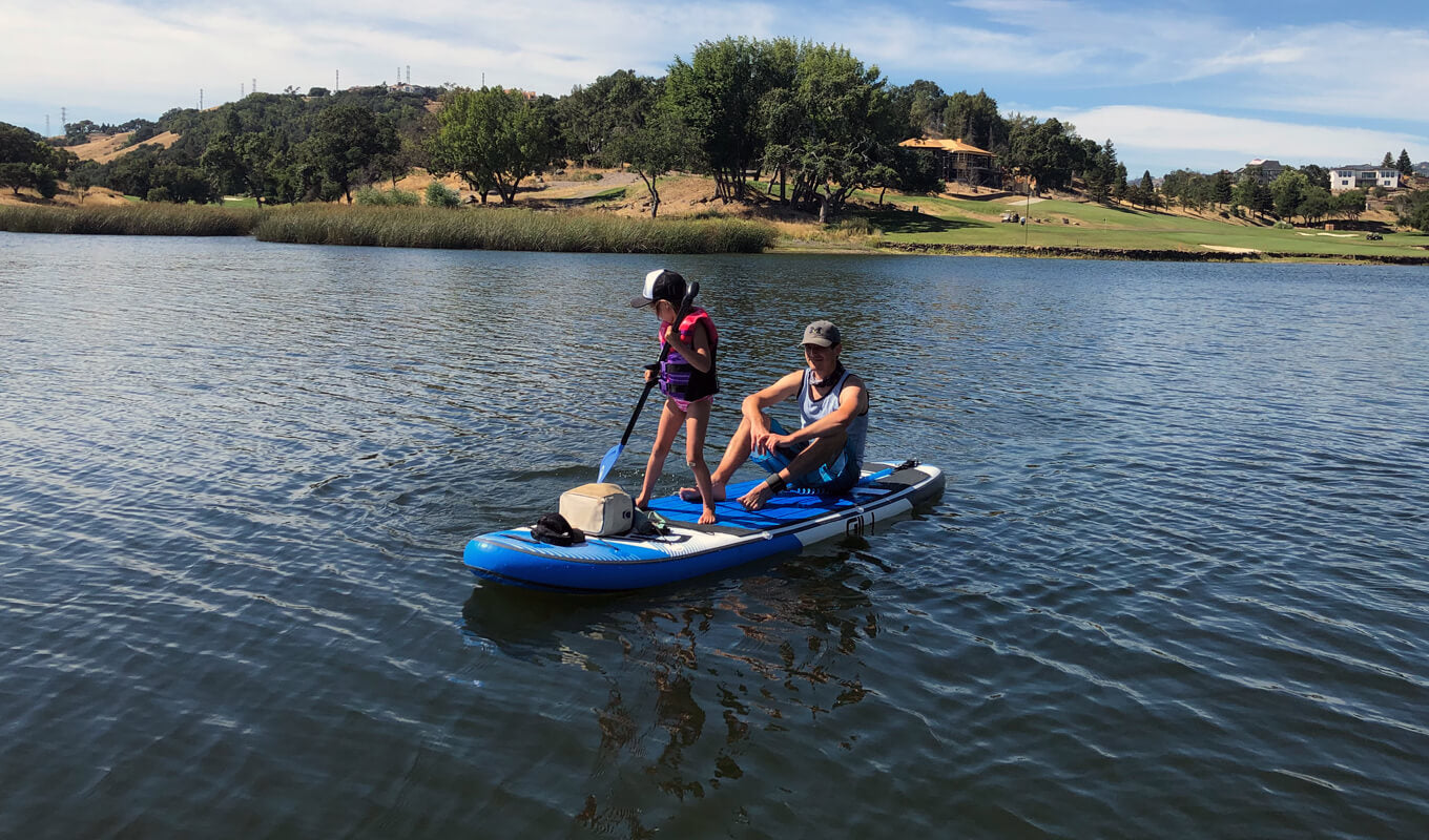 Man and his kid with a life jacket paddle boarding on a lake