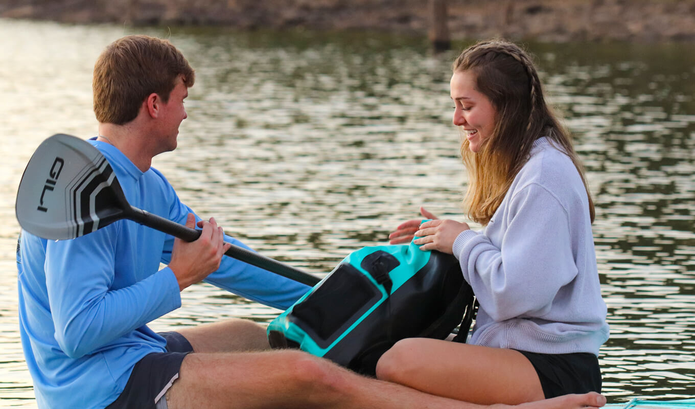 Man and a woman holding a waterproof backpack while paddle boarding