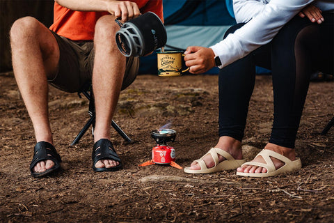 NuuSol-Guy and girl sitting in chairs in the woods pouring coffee wearing NuuSol Sandals