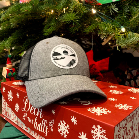 a grey and black Shuswap Soul snapback hat on top of a christmas box infront of a christmas tree