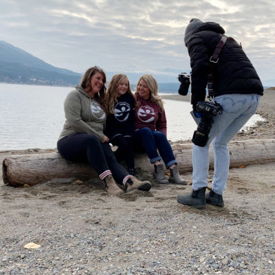 Photographer speaking with 3 people sitting on a log at the beach at Herald Provincial Park in the Shuswap