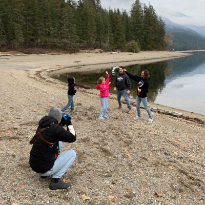 Photographer crouched down on the beach taking pictures of a family on the beach at Herald Park in the Shuswap