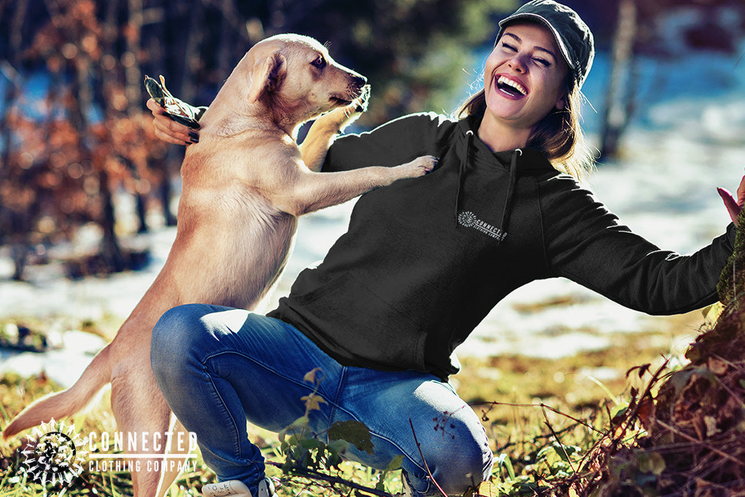 Model wearing Black Show Humanity Unisex Hoodie while smiling and playing with a rescue dog - architectconstructor - Ethically and Sustainably Made - 10% donated to the Society for the Prevention of Cruelty to Animals