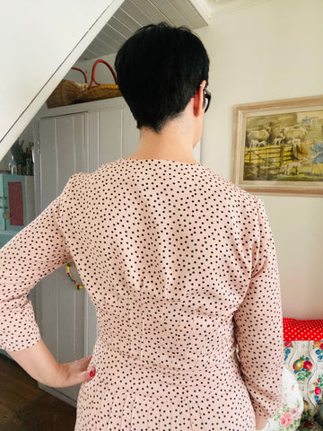 Back view of Lisa in pale pink dress with small black spots, with her hand on her hip