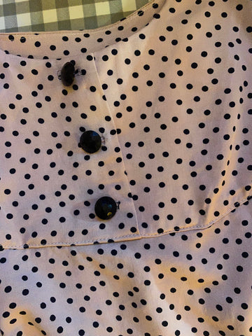 A close up image of pale pink polka dot fabric with small black buttons
