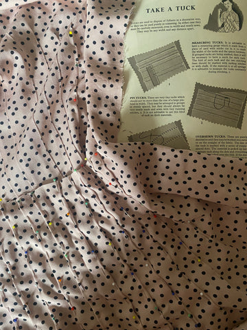 Close up image of pin tucks pinned in fabric and instructions in a book