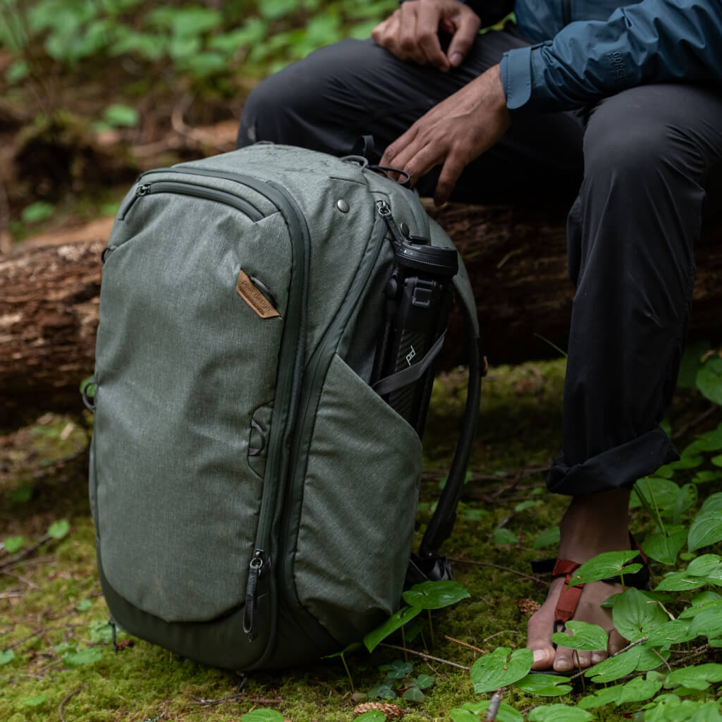Elish sitting on a fallen tree in the woods with his the sage travel bag