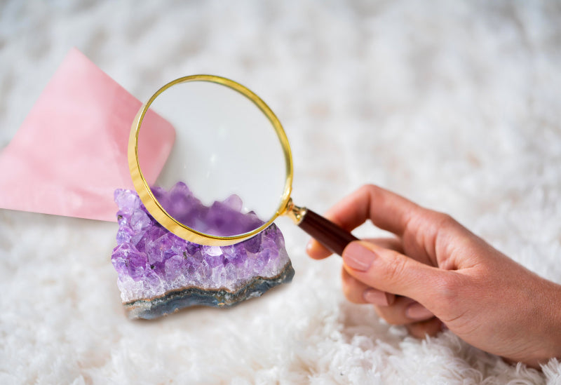 hand holding a hand lens while analyzing crystal rose quartz and amethyst