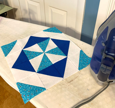 Blue, Teal and White Quilt Block sitting on an ironing board with an iron