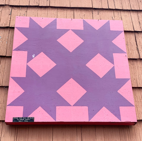 Pink and purple barn quilt hanging on the side of a building.