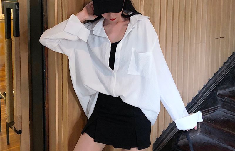 Casual-chic in oversized white shirt, skirt, and cap indoors.