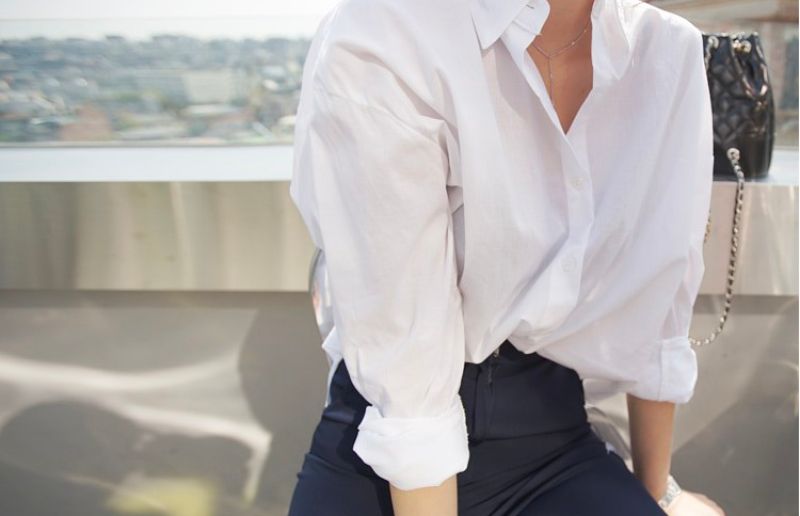 Chic white linen shirt and dark trousers outfit, accessorized with a quilted bag.