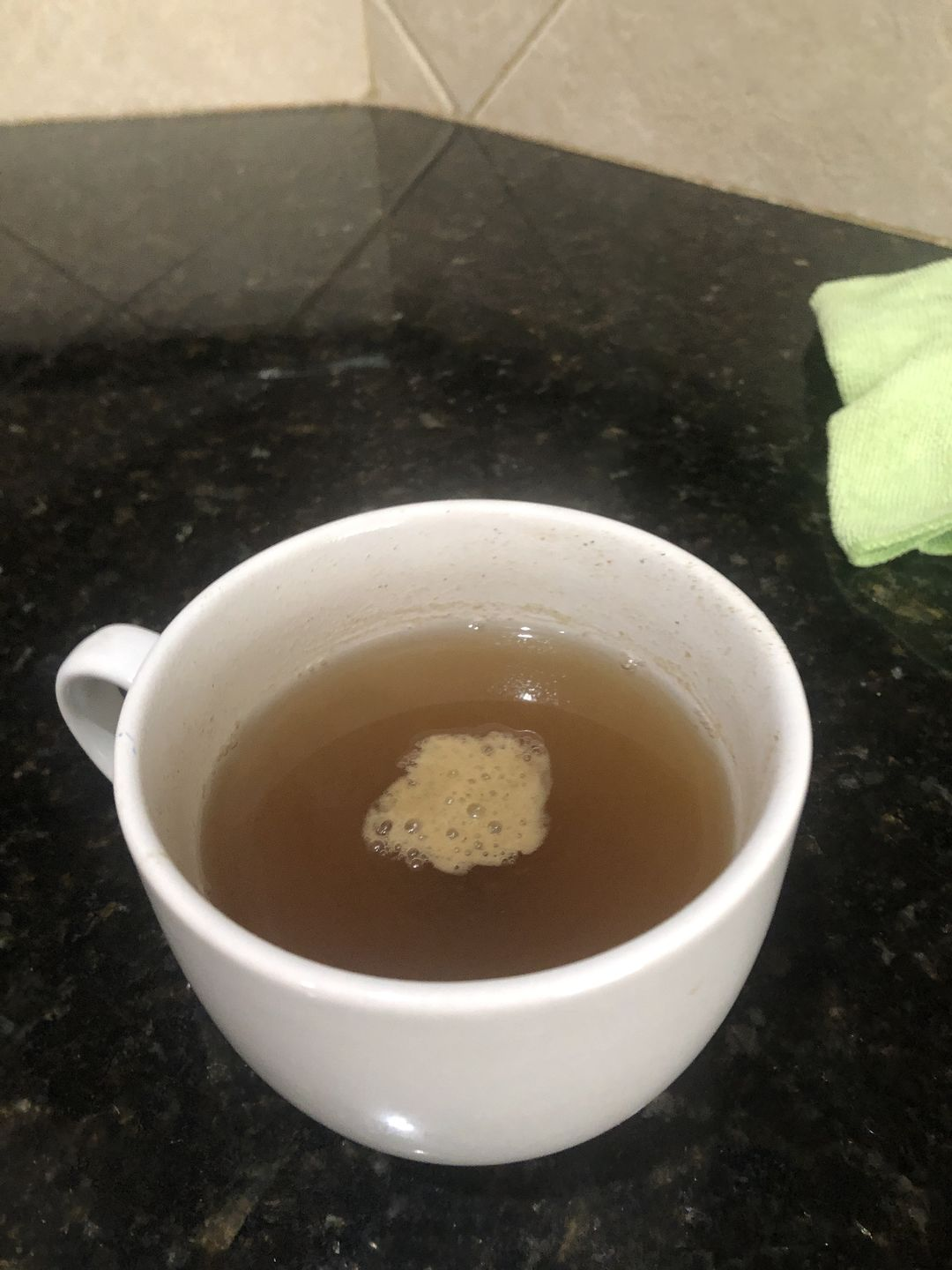 A white cup filled with brown liquid and foam on a dark countertop.