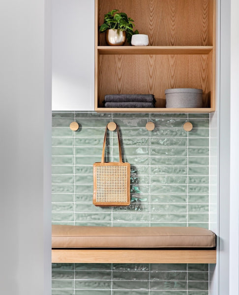 A mudroom featuring green tiles, bag hooks, a leather bench seat and storage cupboards