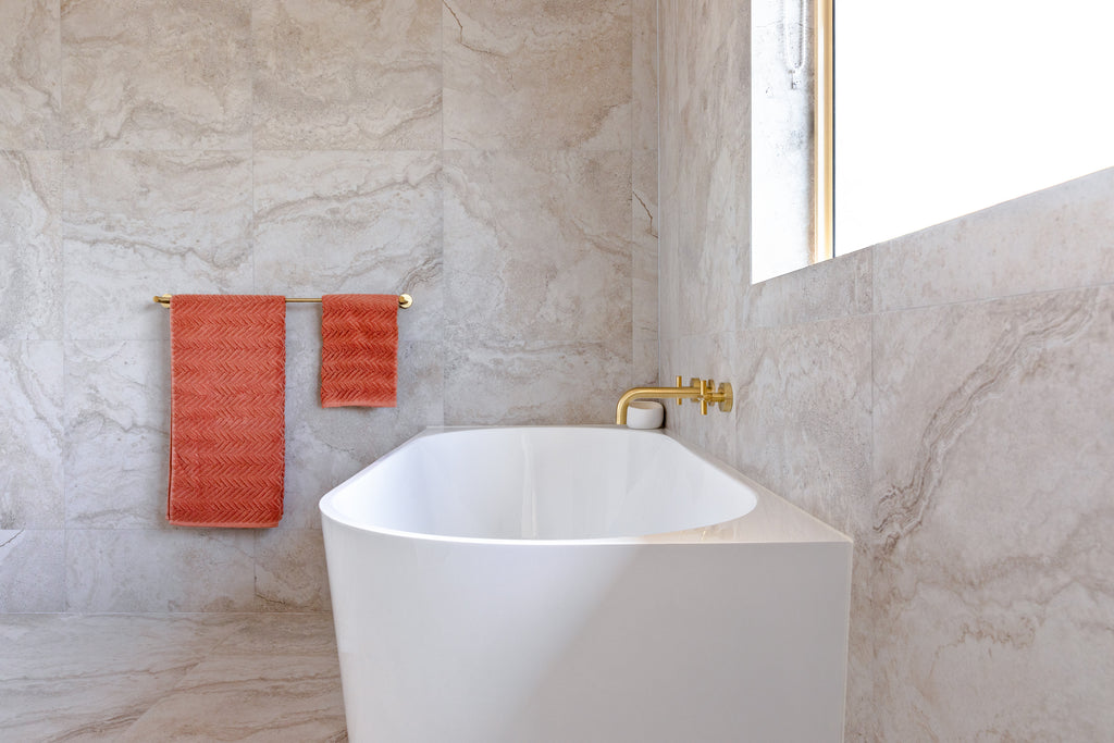 Bathroom featuring a bath in the middle, brushed brass tapware and hanging orange towels.